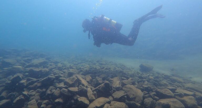 Diver hovering over rocky lake bottom.