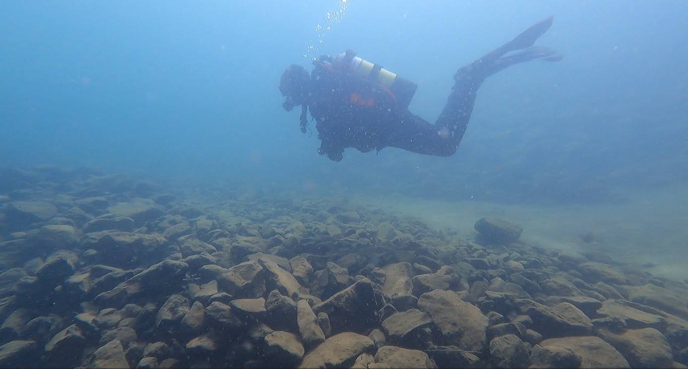 Diver hovering over rocky lake bottom.